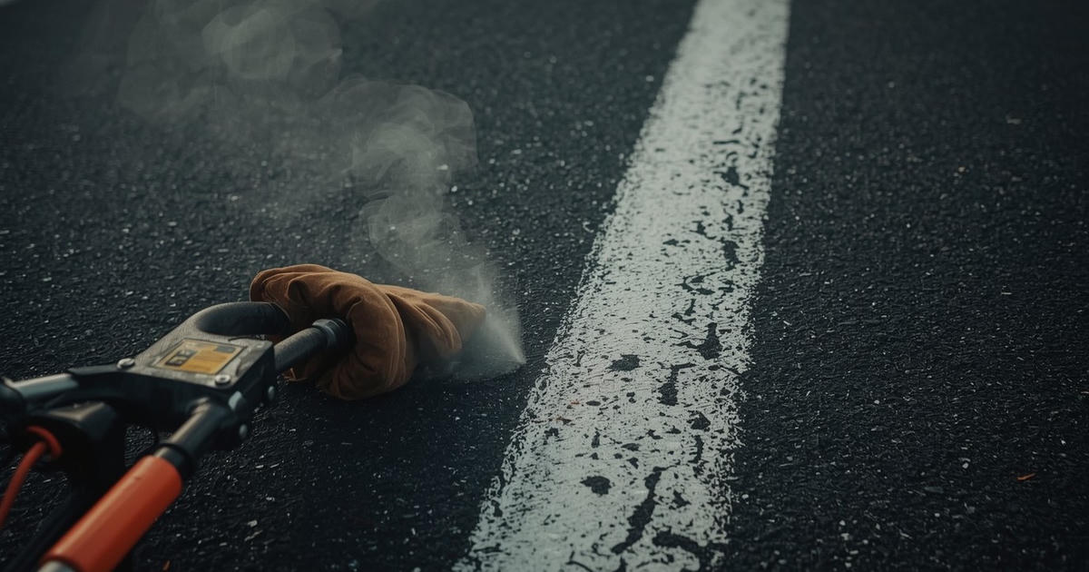 A worn work glove rests on a paint striper beside a fresh white line on warm black asphalt in soft morning light.